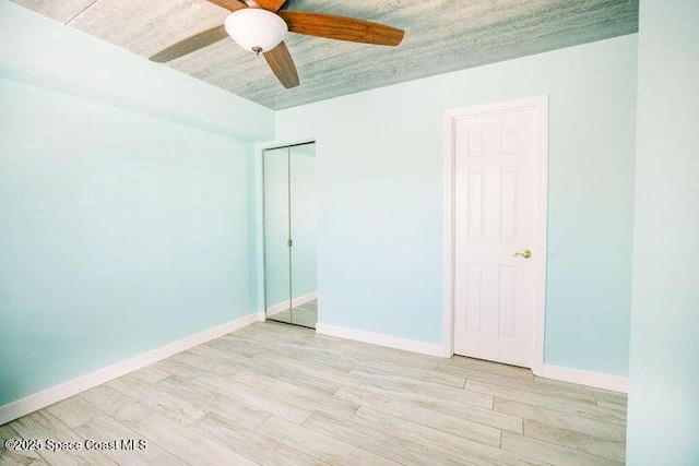 unfurnished bedroom featuring a ceiling fan, baseboards, a closet, and light wood-style flooring