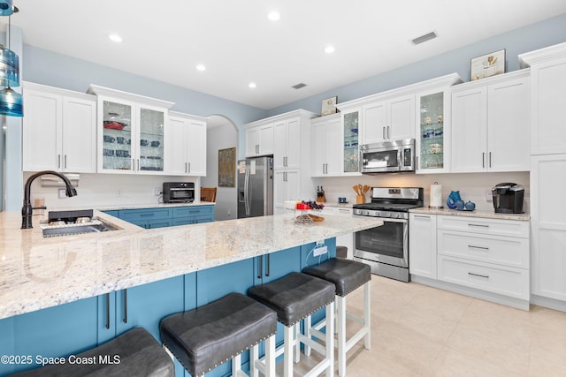 kitchen with a kitchen breakfast bar, white cabinets, a sink, stainless steel appliances, and a peninsula