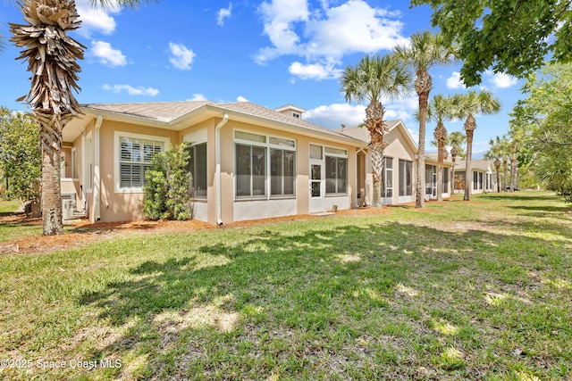 rear view of property featuring stucco siding, a yard, and a sunroom