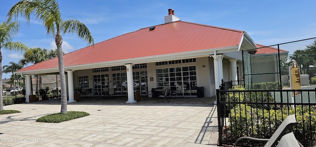 exterior space featuring a chimney, stucco siding, fence, metal roof, and a patio area