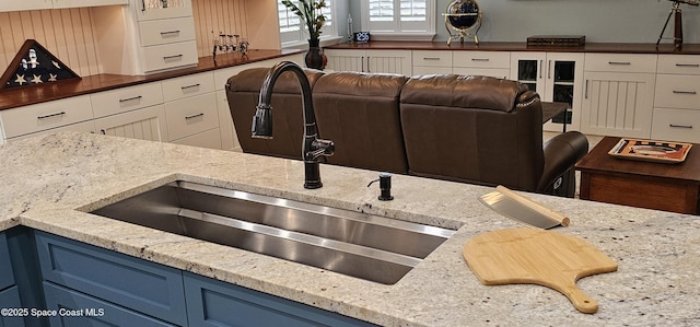 kitchen with light stone counters, blue cabinetry, white cabinets, and a sink