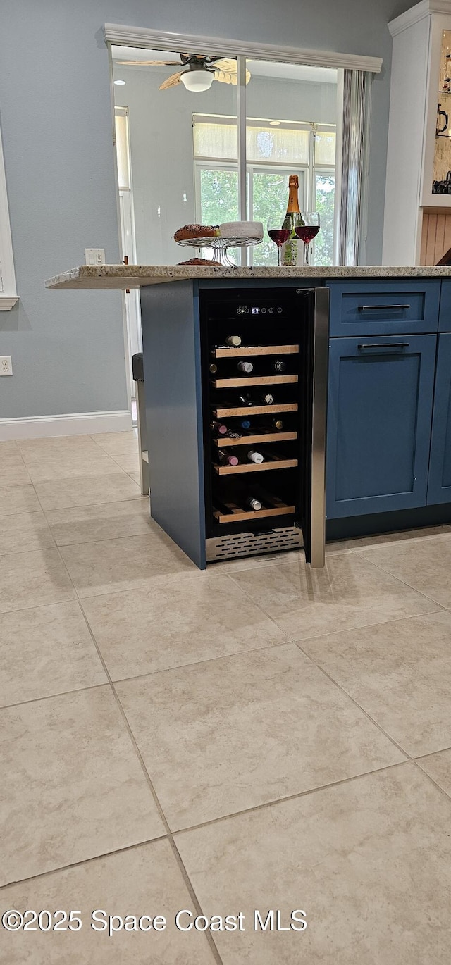 bar featuring wine cooler, light tile patterned flooring, ceiling fan, baseboards, and a dry bar