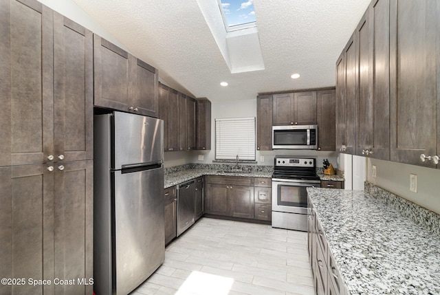 kitchen featuring a sink, a skylight, dark brown cabinetry, a textured ceiling, and appliances with stainless steel finishes