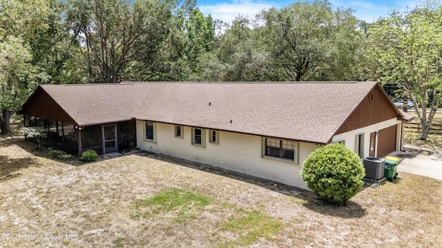 back of house featuring concrete driveway, roof with shingles, central air condition unit, stucco siding, and a sunroom