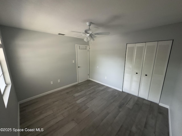 unfurnished bedroom with dark wood finished floors, visible vents, a closet, baseboards, and ceiling fan