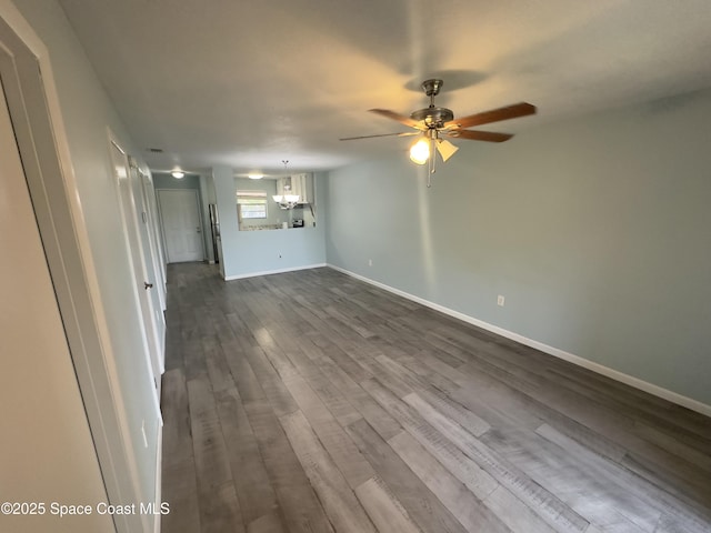unfurnished living room featuring ceiling fan with notable chandelier, baseboards, and dark wood finished floors