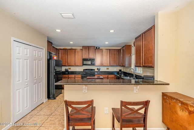 kitchen with a sink, dark stone countertops, a peninsula, visible vents, and black appliances