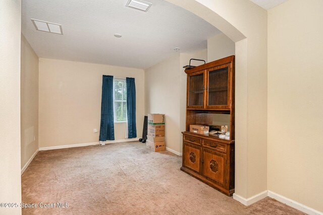 empty room featuring arched walkways, light colored carpet, visible vents, and baseboards
