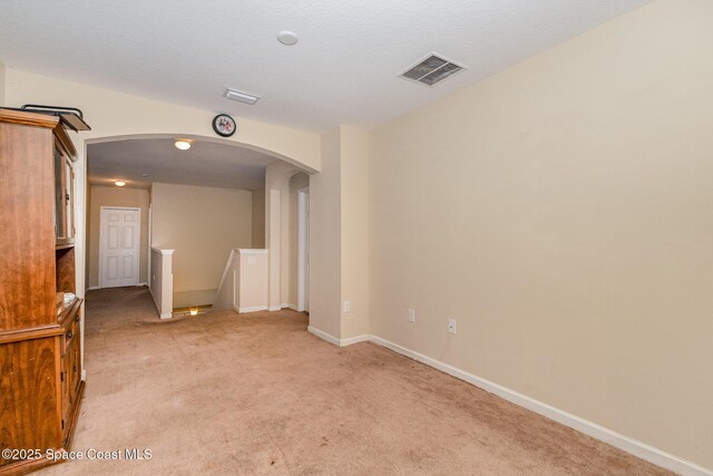 unfurnished room featuring arched walkways, light colored carpet, visible vents, and baseboards