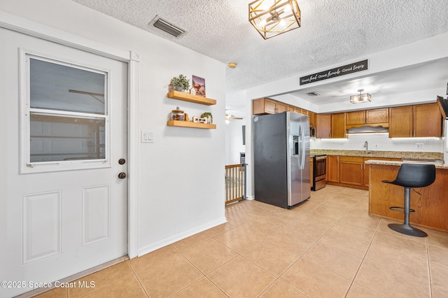 kitchen featuring stainless steel appliances, visible vents, brown cabinetry, light countertops, and a breakfast bar