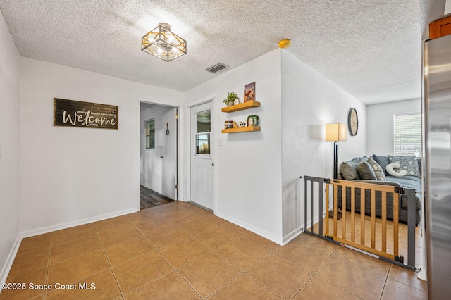 hallway featuring light tile patterned flooring, a textured ceiling, visible vents, and baseboards