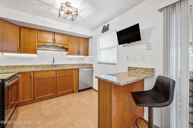 kitchen with a peninsula, a breakfast bar area, a sink, brown cabinets, and appliances with stainless steel finishes