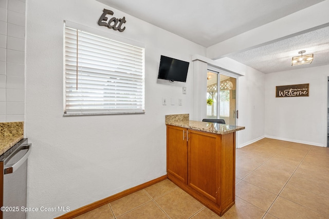 kitchen with a peninsula, baseboards, light stone counters, brown cabinetry, and light tile patterned floors