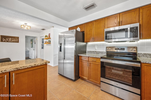 kitchen with stainless steel appliances, visible vents, light tile patterned floors, decorative backsplash, and brown cabinetry