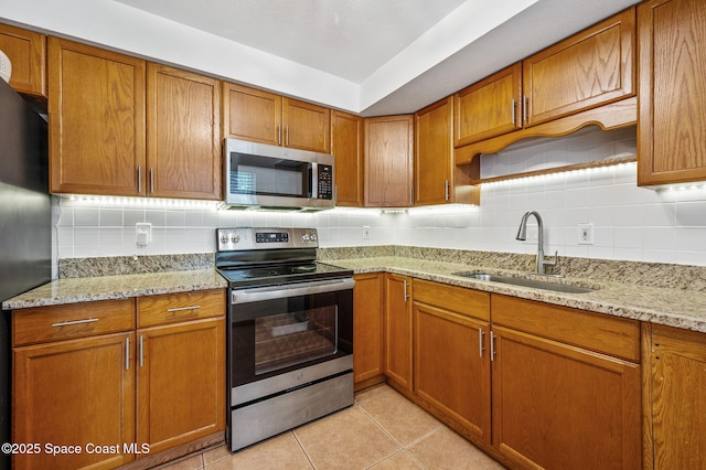kitchen featuring brown cabinetry, a sink, appliances with stainless steel finishes, and tasteful backsplash