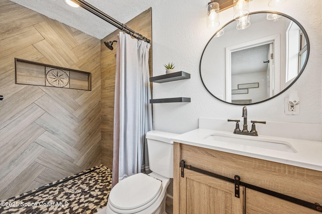 bathroom featuring a tile shower, toilet, vanity, and a textured ceiling