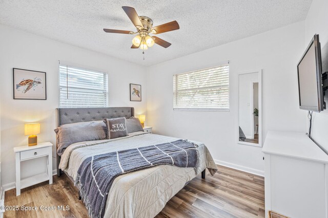 bedroom featuring baseboards, wood finished floors, multiple windows, and a textured ceiling