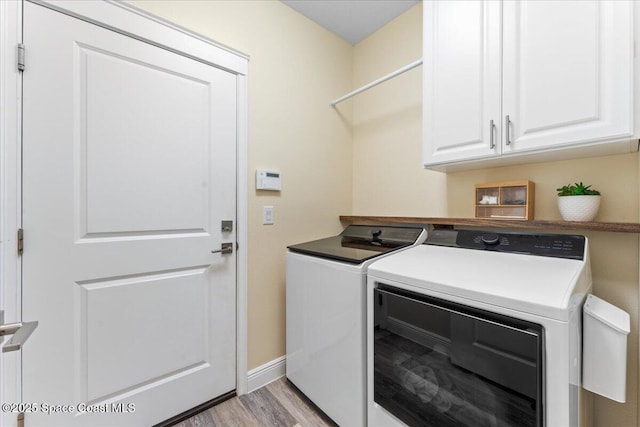 clothes washing area featuring cabinet space, washing machine and dryer, light wood finished floors, and baseboards