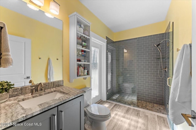 bathroom featuring toilet, wood finished floors, vanity, and a stall shower