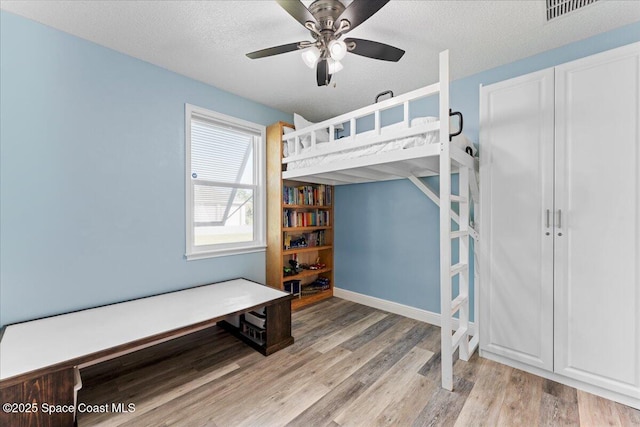 bedroom featuring light wood finished floors, visible vents, a ceiling fan, baseboards, and a textured ceiling