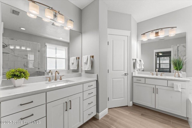 full bathroom with two vanities, wood finished floors, a marble finish shower, and a sink