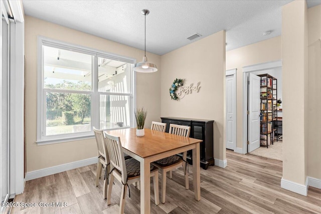 dining area featuring visible vents, light wood-style flooring, baseboards, and a textured ceiling