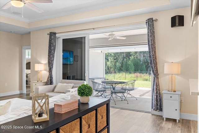 living area with light wood-style floors, ceiling fan, a tray ceiling, baseboards, and ornamental molding