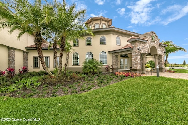 view of front of home featuring a tiled roof, stone siding, a front yard, and stucco siding