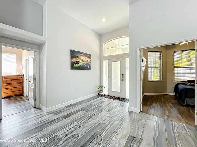 entryway featuring baseboards, light wood-style flooring, a high ceiling, and recessed lighting