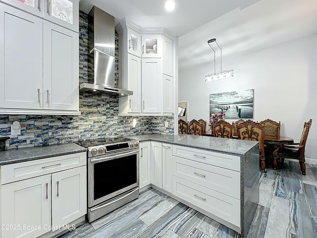 kitchen with a peninsula, electric range, white cabinetry, decorative backsplash, and wall chimney range hood