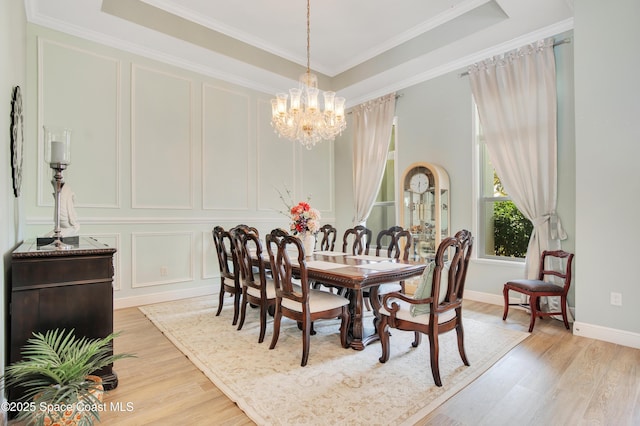 dining area featuring a decorative wall, light wood finished floors, a notable chandelier, and a tray ceiling