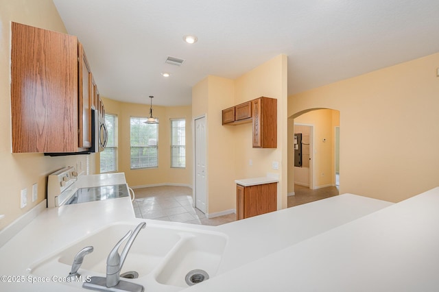 6921 Abbeyville Rd, Melbourne, FL 32940 - kitchen featuring light tile patterned floors, brown cabinets, range, arched walkways, and decorative light fixtures