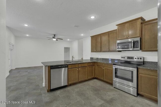 kitchen with brown cabinets, appliances with stainless steel finishes, a sink, a ceiling fan, and a peninsula