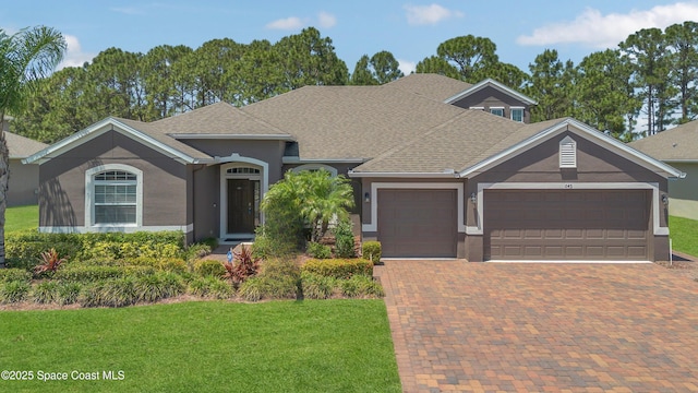 view of front facade featuring a garage, a front yard, decorative driveway, stucco siding, and a shingled roof