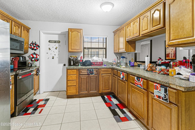 kitchen with brown cabinetry, stainless steel appliances, a textured ceiling, and a sink