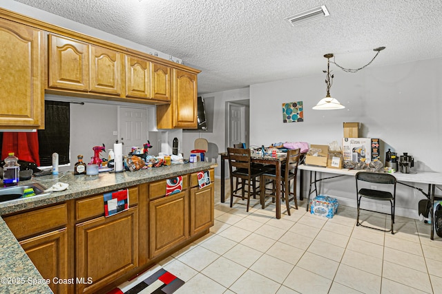 kitchen with visible vents, light tile patterned flooring, decorative light fixtures, brown cabinetry, and a textured ceiling