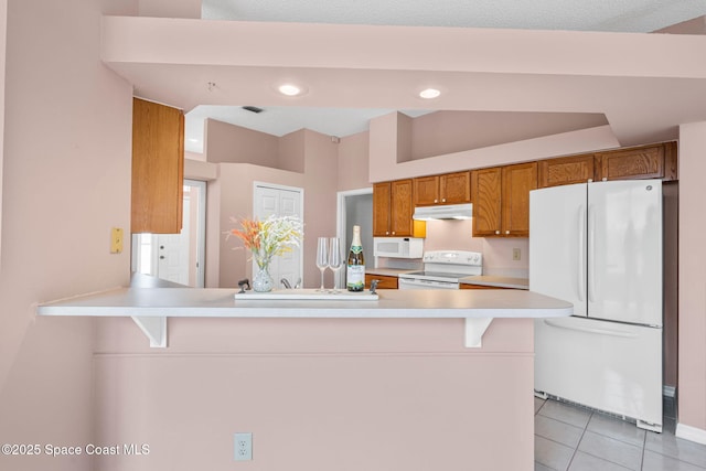 kitchen with white appliances, brown cabinets, under cabinet range hood, light countertops, and light tile patterned floors