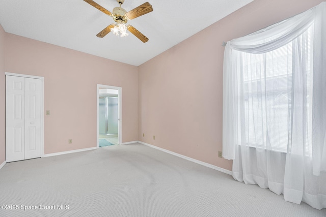 unfurnished bedroom featuring light colored carpet, ensuite bathroom, baseboards, and a ceiling fan