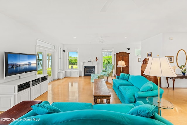 living room featuring a ceiling fan, a glass covered fireplace, recessed lighting, and light wood finished floors