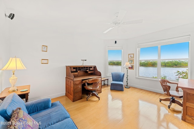 office featuring a water view, baseboards, ceiling fan, and light wood-type flooring