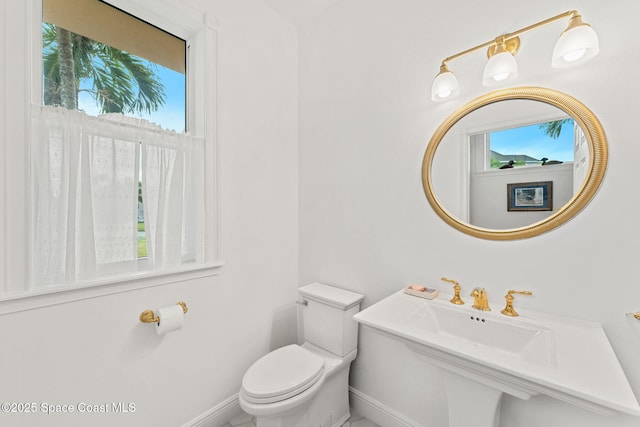half bathroom featuring toilet, baseboards, and a wealth of natural light
