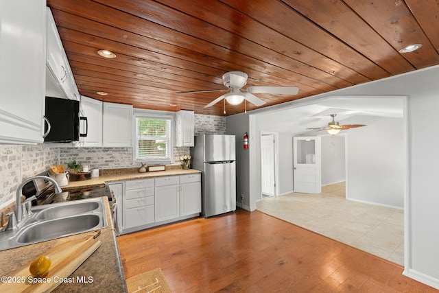 kitchen featuring black microwave, a sink, freestanding refrigerator, a ceiling fan, and wooden ceiling