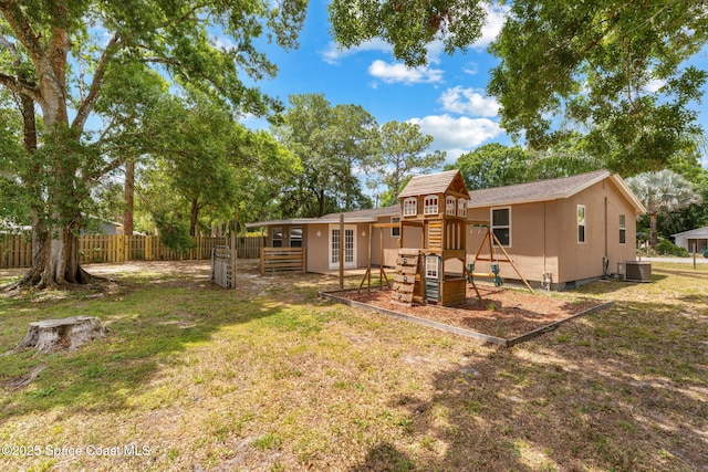 rear view of house with a yard, fence, central AC unit, and a playground