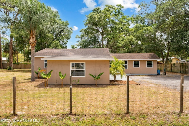 ranch-style home featuring fence, stucco siding, roof with shingles, and a front yard