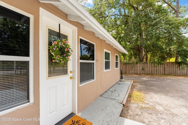 doorway to property featuring fence and stucco siding