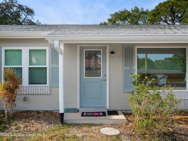 entrance to property featuring stucco siding and roof with shingles