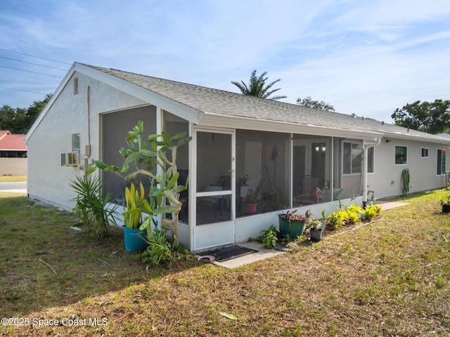 rear view of property with a lawn, roof with shingles, stucco siding, and a sunroom