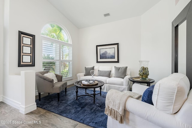 living room featuring lofted ceiling, visible vents, baseboards, and wood finished floors