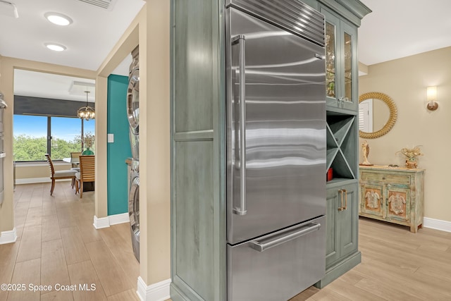 kitchen featuring glass insert cabinets, light wood-style floors, built in fridge, green cabinets, and baseboards