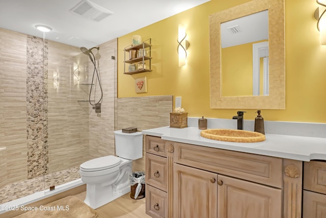 full bathroom with visible vents, toilet, a tile shower, and vanity
